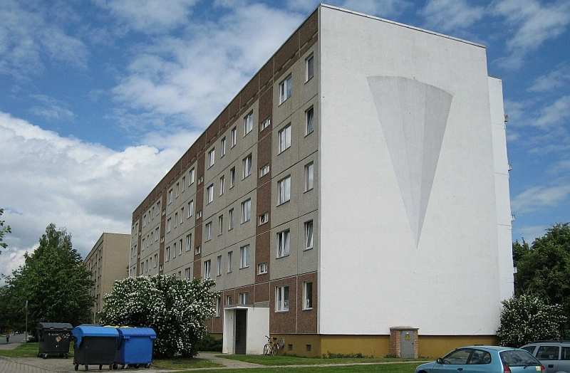 Ein Mehrfamilienhaus mit einer hellen Fassade und weißen Fenstern, umgeben von Grünflächen.