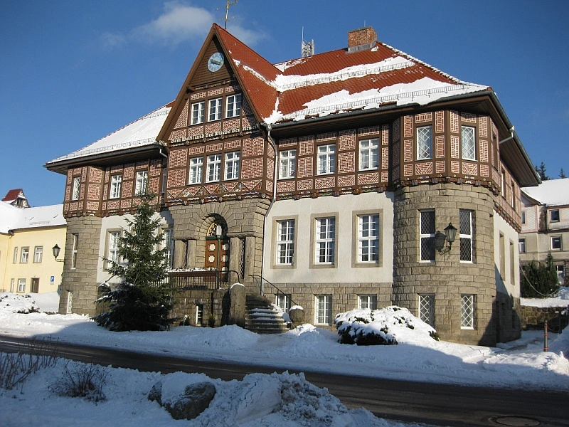 Ein historisches Gebäude mit Fachwerk und einem roten Ziegeldach ist von Schnee bedeckt. Der Himmel ist blau mit einigen weißen Wolken.