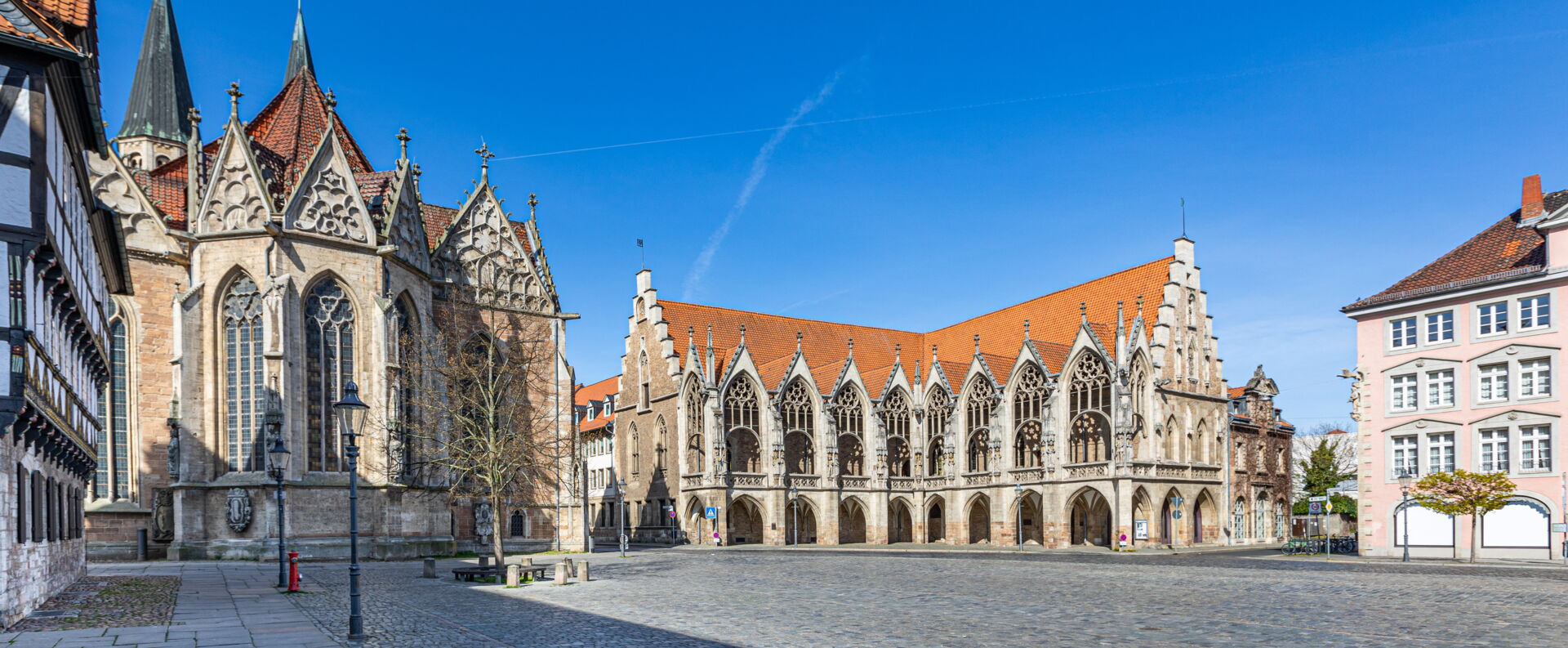 Ein sonniger Blick auf einen historischen Marktplatz mit einem Rathaus im gotischen Stil und weiteren historischen Gebäuden unter einem klaren blauen Himmel.