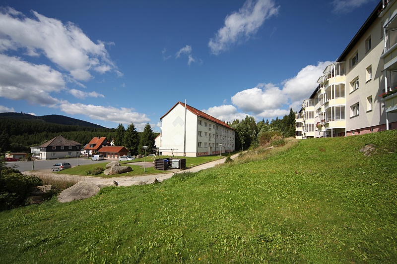 Eine Wohnanlage mit mehreren Mehrfamilienhäusern, umgeben von viel Grünfläche mit Bäumen und Büschen unter einem leicht bewölkten Himmel.
